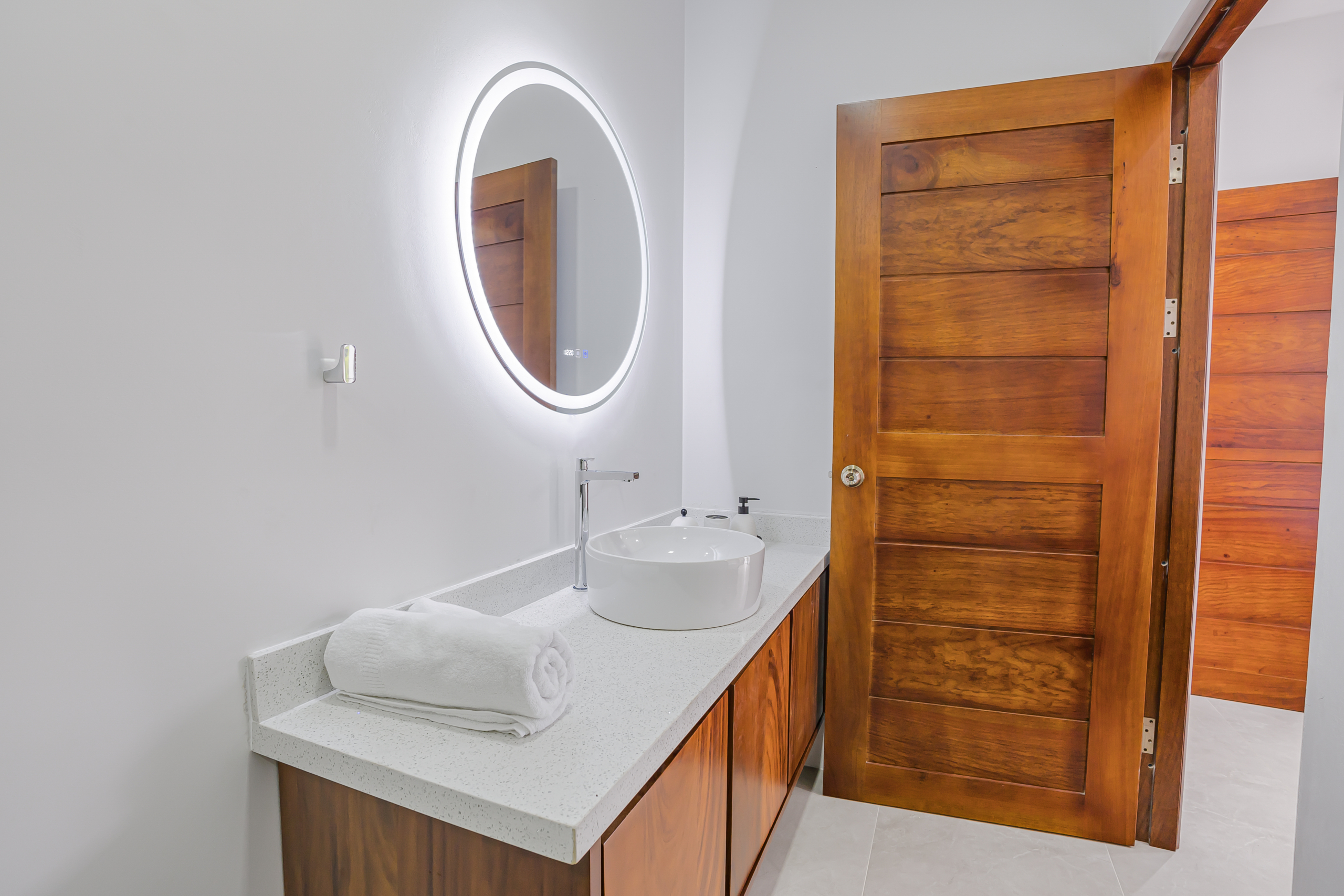 Bathroom vanity with round LED mirror and wood cabinetry at home in La Fortuna, Costa Rica